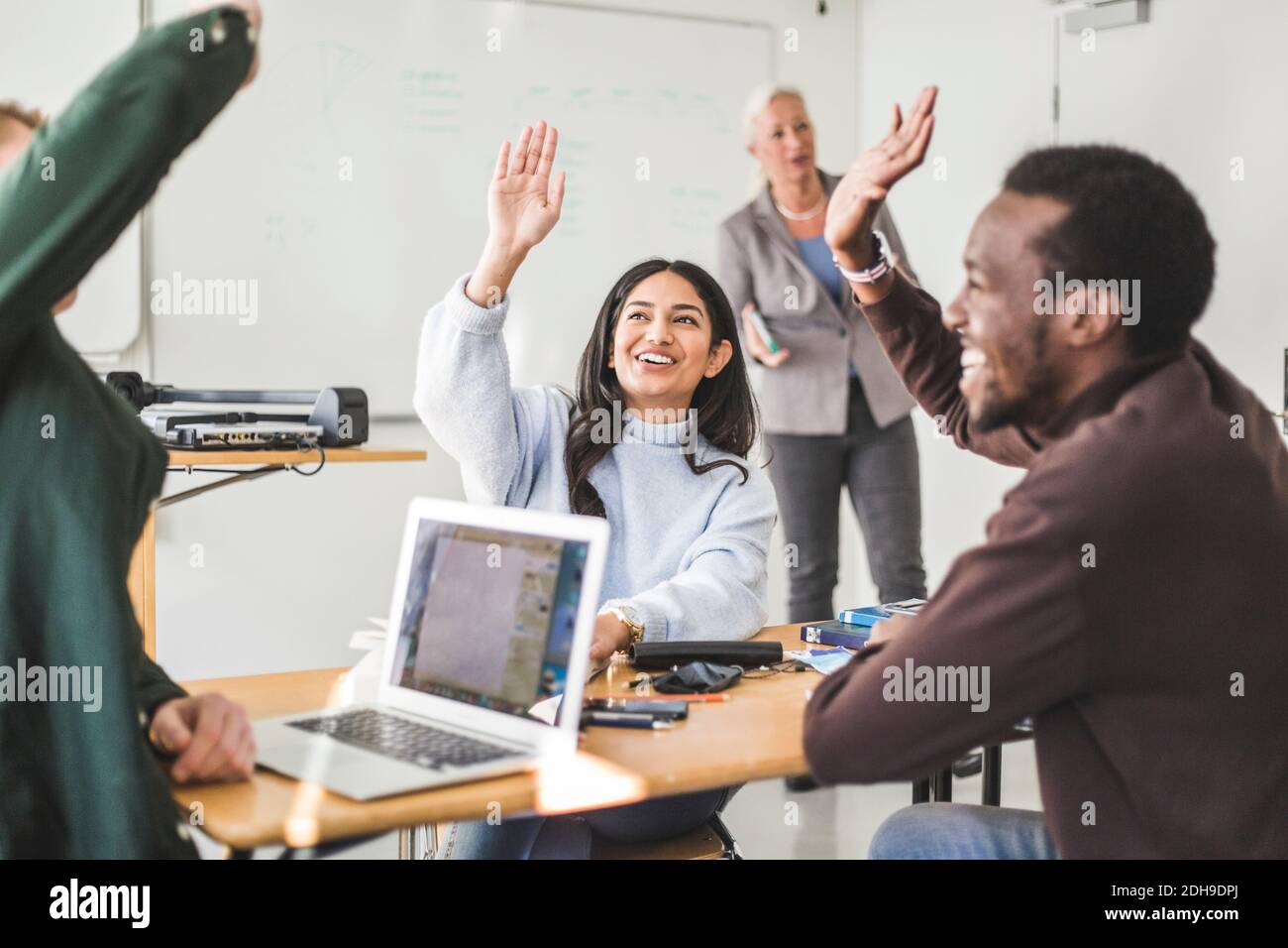 Lächelnde junge Frau und Freunde, die im Klassenzimmer die Hände heben Stockfoto