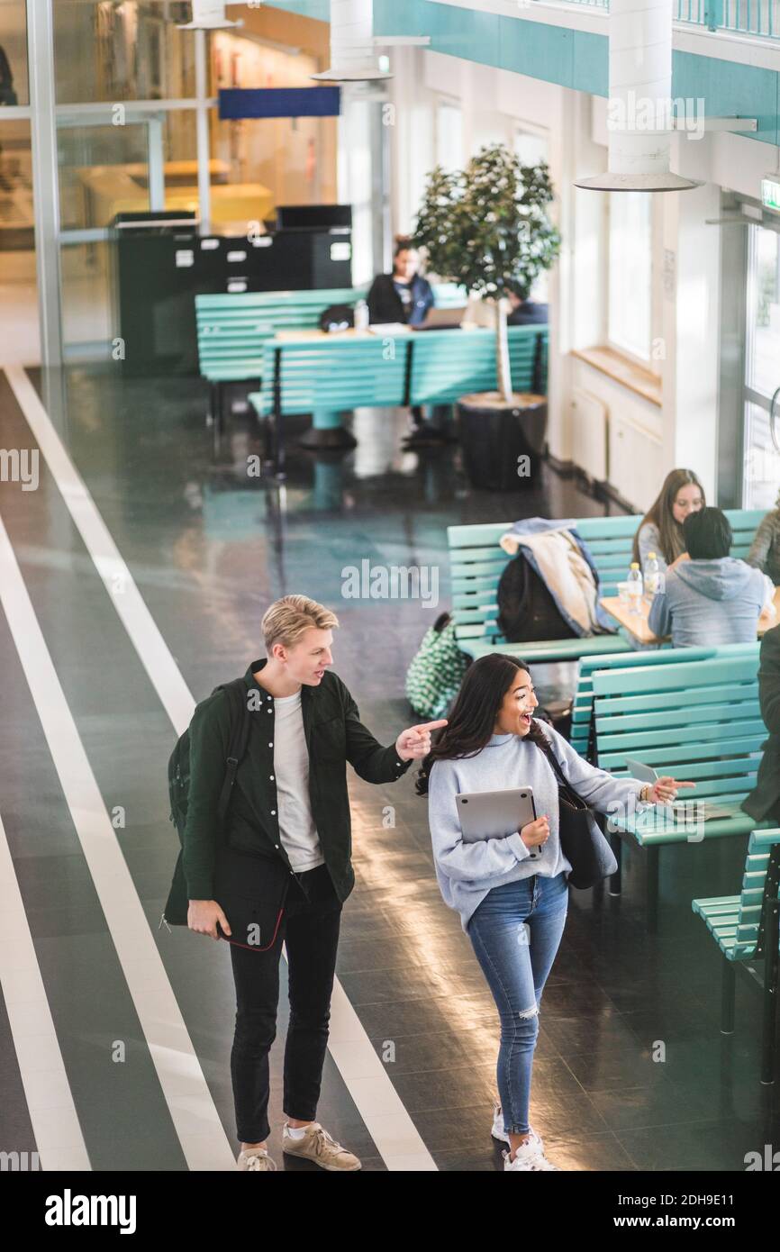 Männliche und weibliche Studenten zeigen beim Gehen in der Cafeteria an universität Stockfoto