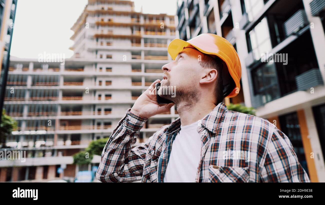 Porträt eines jungen Handwerkers, der beim Stehen auf der Baustelle anruft. Techniker, der auf einer Baustelle telefoniert Stockfoto