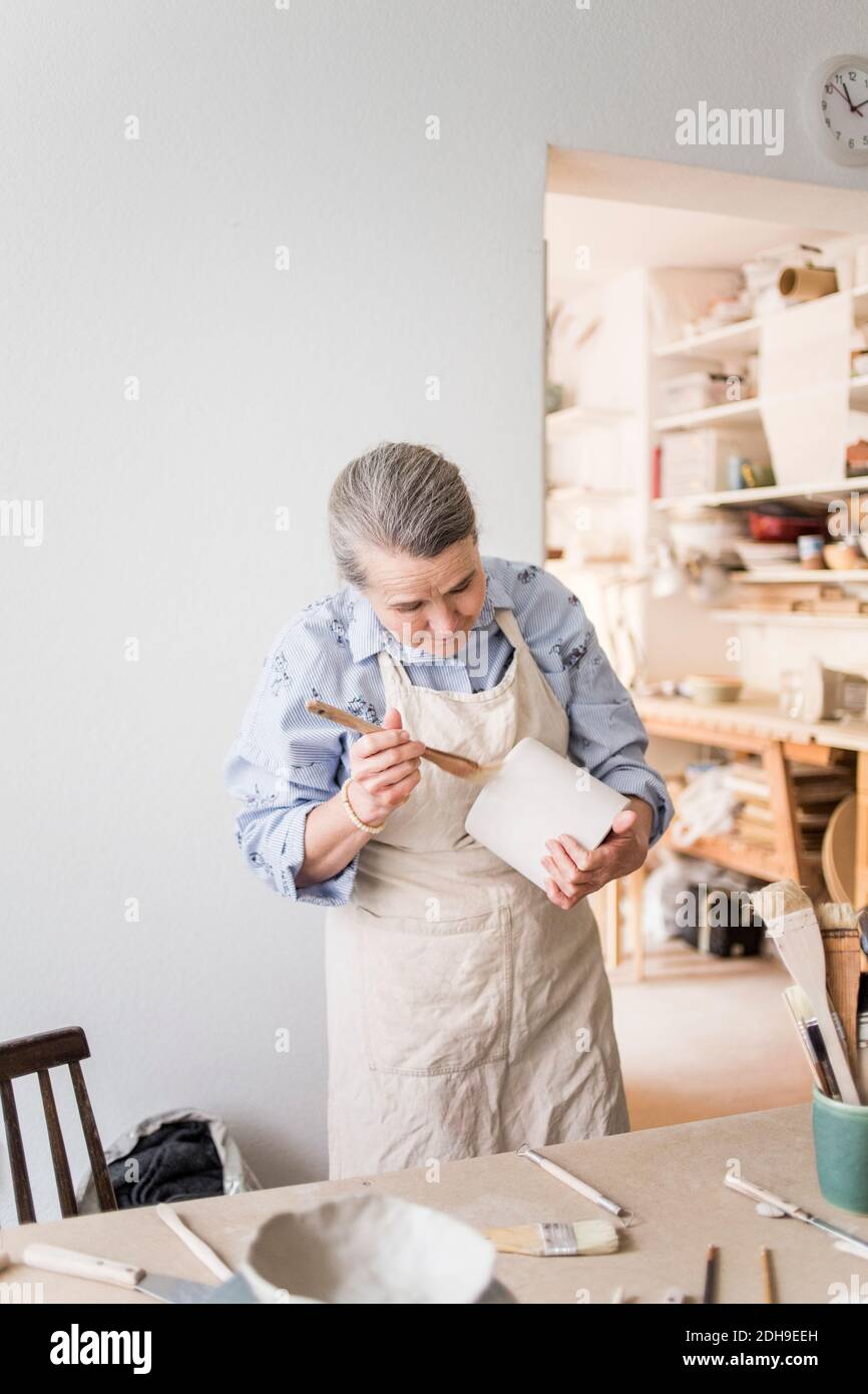 Ältere weibliche Töpfer mit Pinsel auf Vase von Tisch an Werkstatt Stockfoto