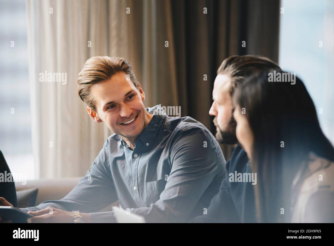 Glücklicher Geschäftsmann im Gespräch mit Kollegen in hell erleuchteten Büro Stockfoto