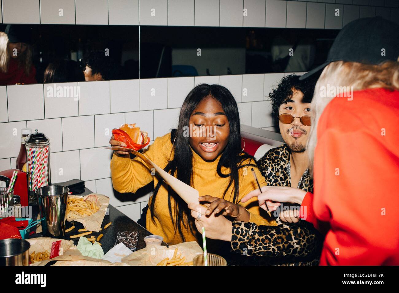 Kellnerin zeigt, während Frau mit Burger Essen von Freund bestellen Im Café Stockfoto