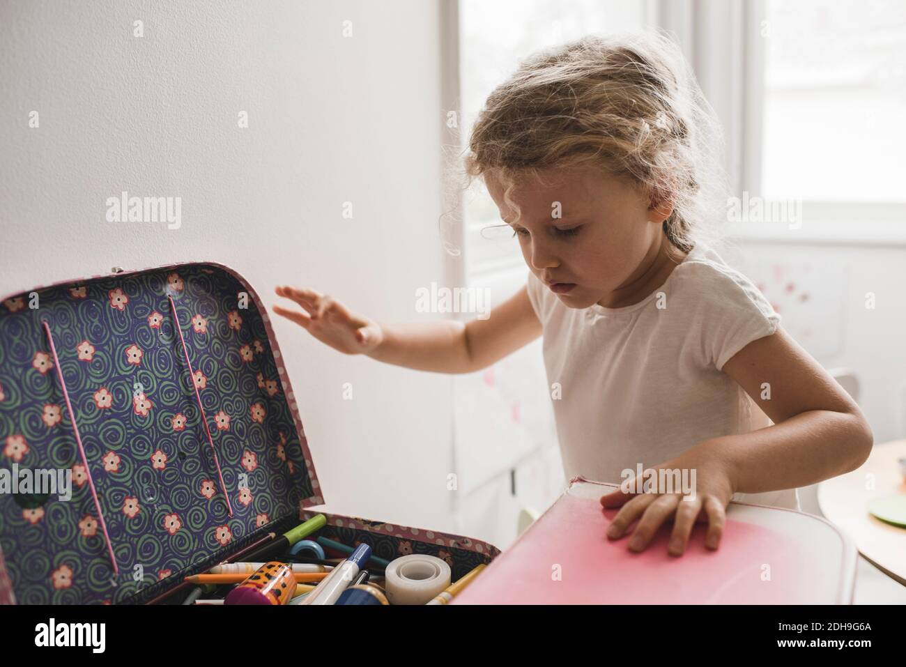 Mädchen auf der Suche nach Spielzeug im Koffer im Spielzimmer Stockfoto