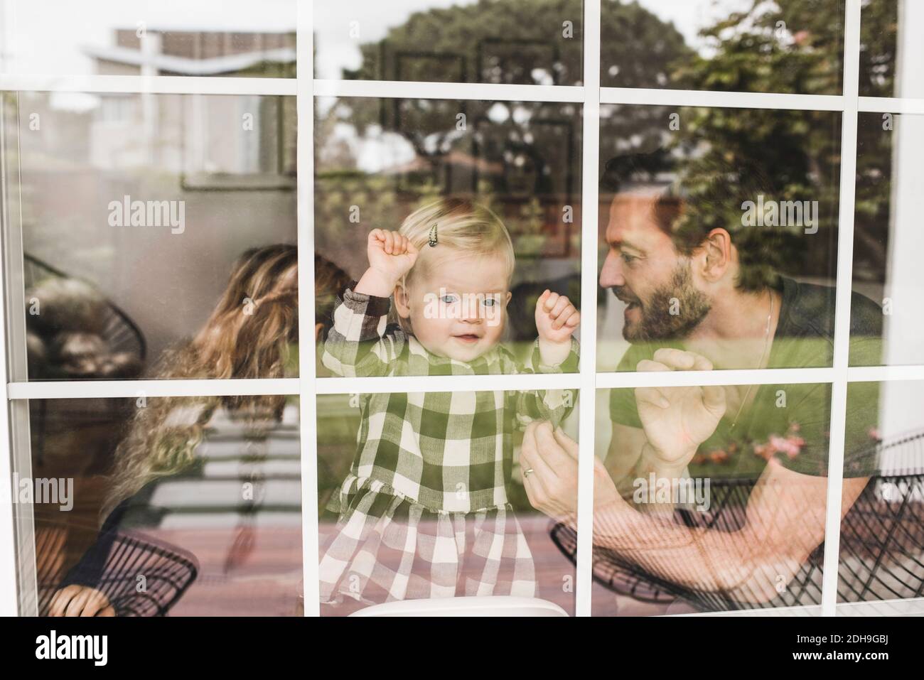 Mittelerwachsener Mann mit Töchtern, die durch das Fenster des Hauses gesehen werden Stockfoto Mittelerwachsener Mann mit Töchtern, die durch das Fenster des Hauses gesehen werden Stockfoto