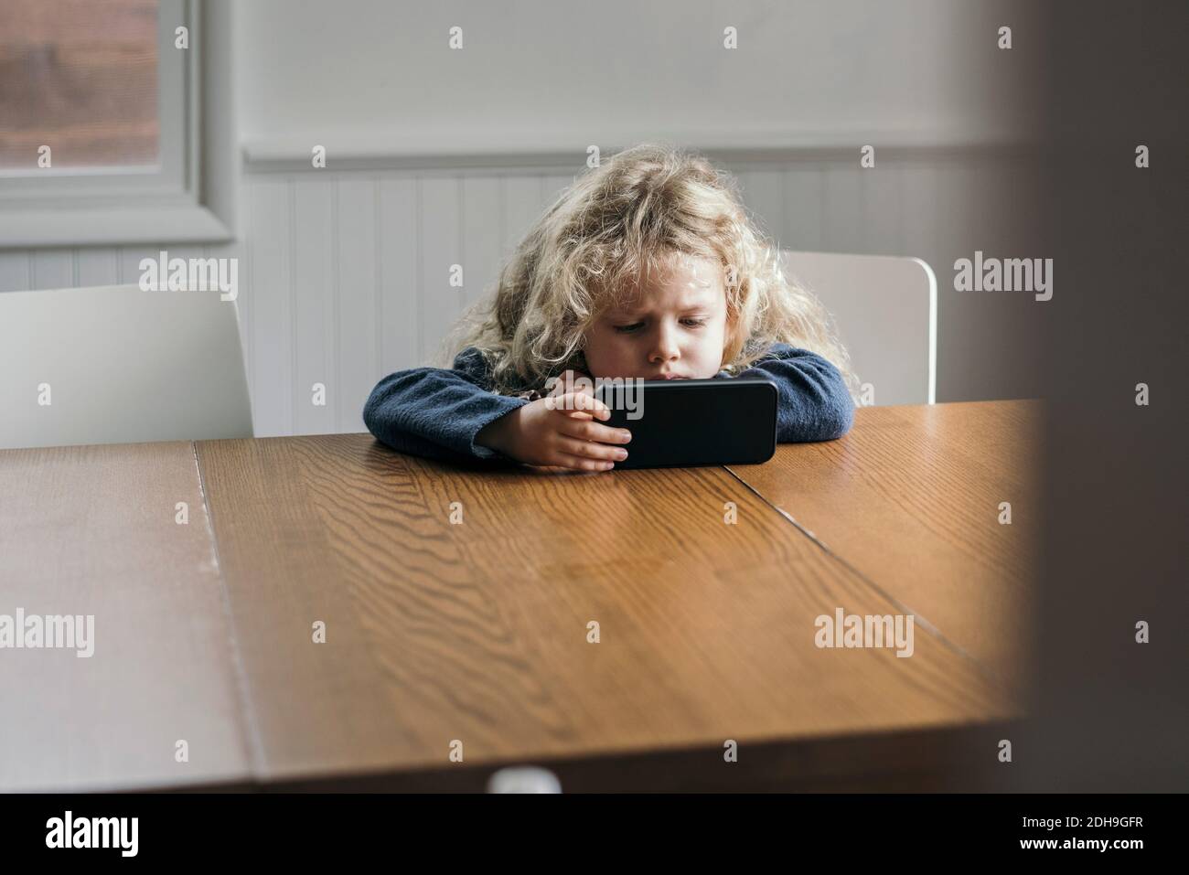 Mädchen mit Handy am Tisch im Haus Stockfoto