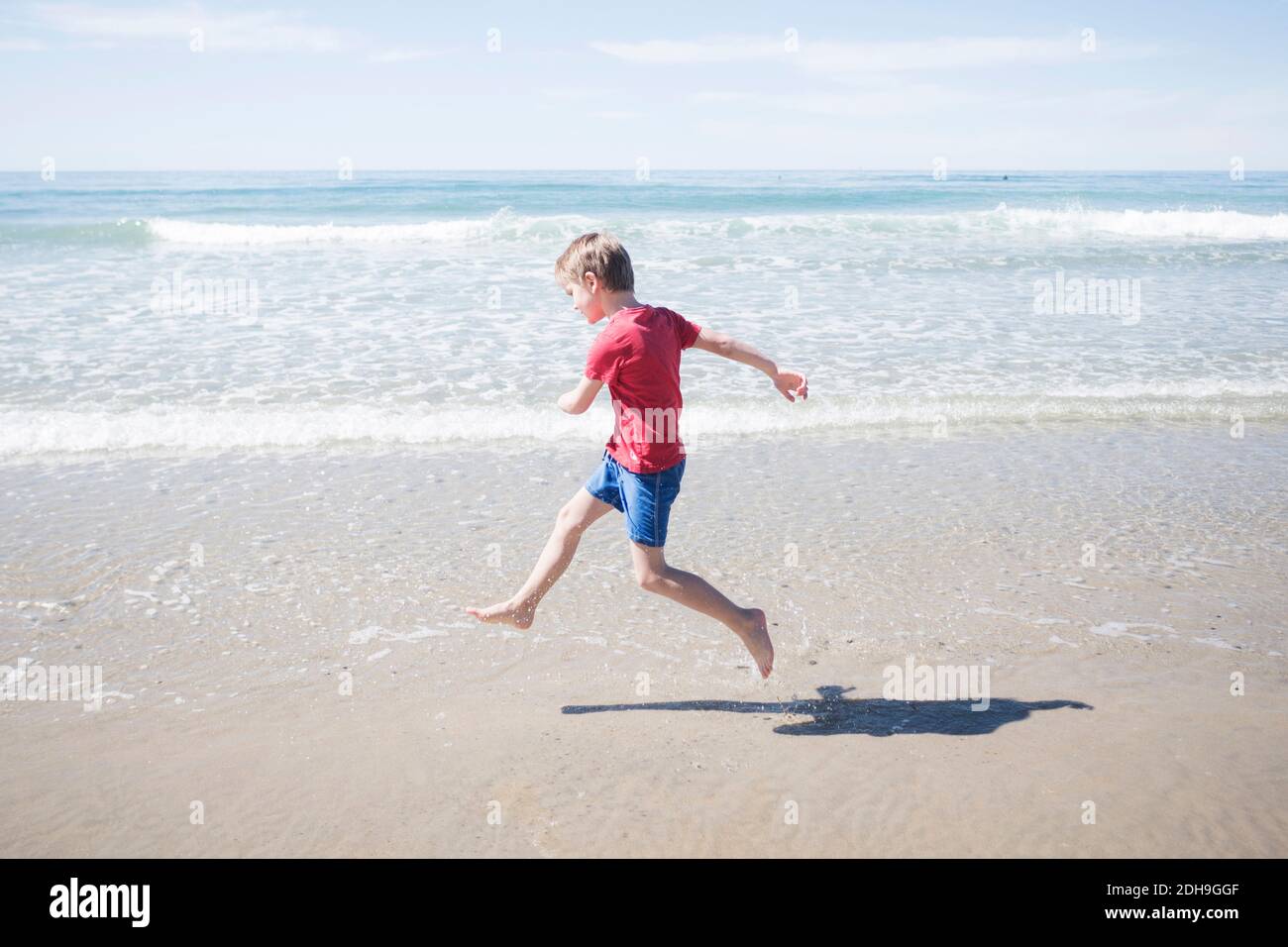 Volle Länge Seitenansicht des Jungen am Strand laufen Sonniger Tag Stockfoto
