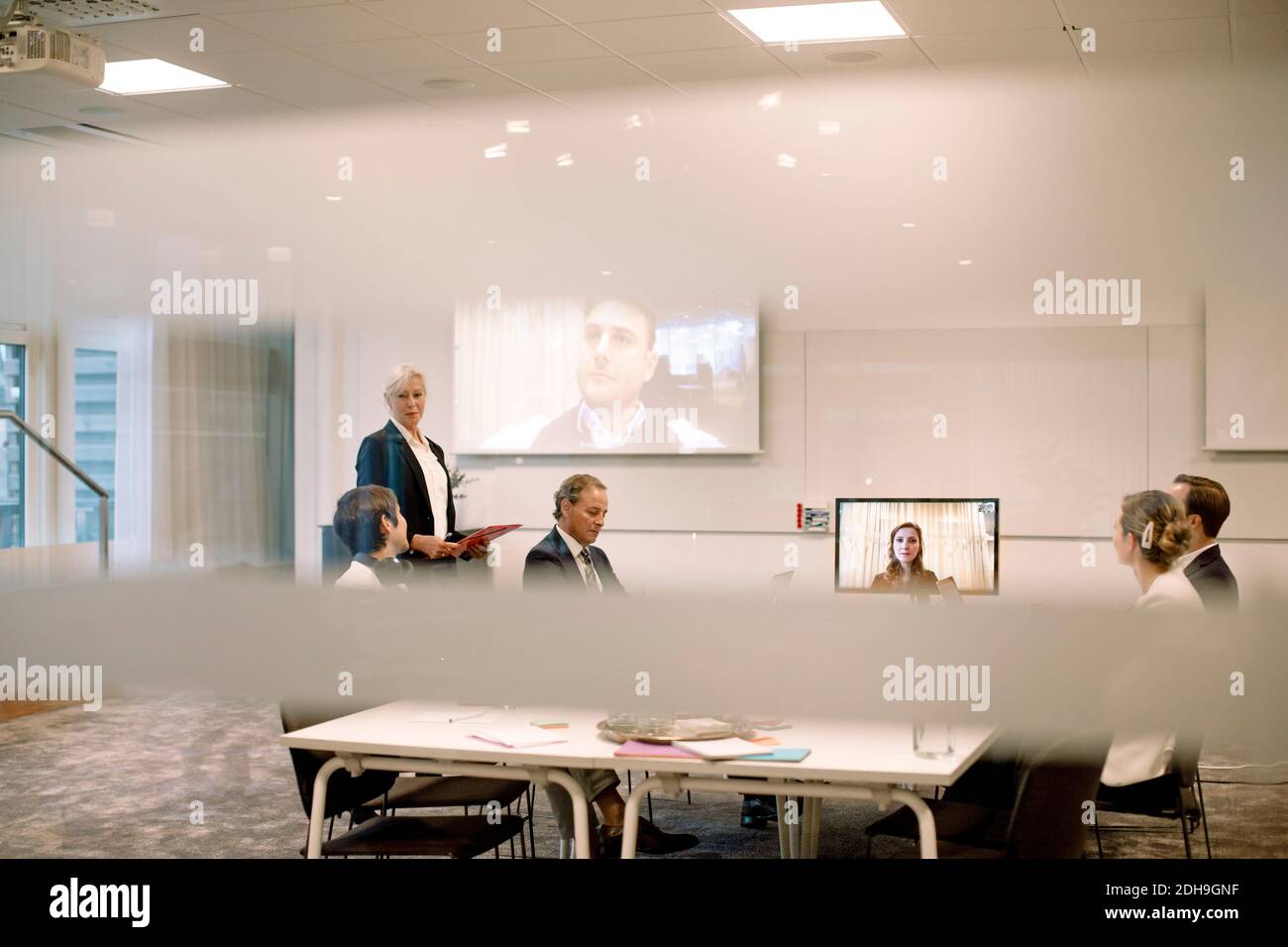 Männliche und weibliche Führungskräfte diskutieren in Web-Konferenz Sitzung gesehen Durch Glas am Arbeitsplatz Stockfoto