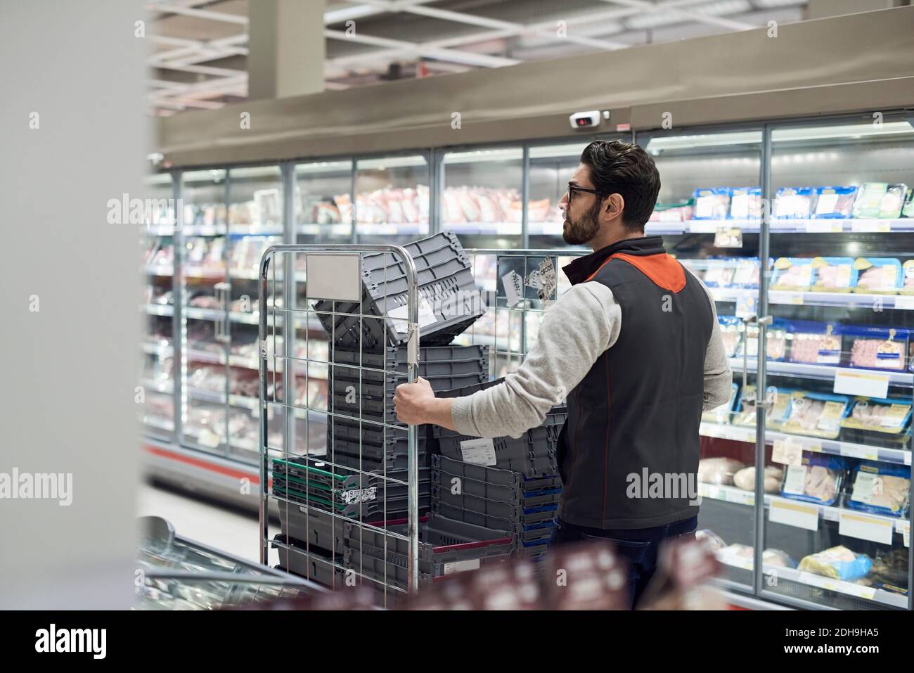 Rückansicht des Verkäufers, der den Wagen mit Kunststoffkisten schiebt Im Supermarkt Stockfoto