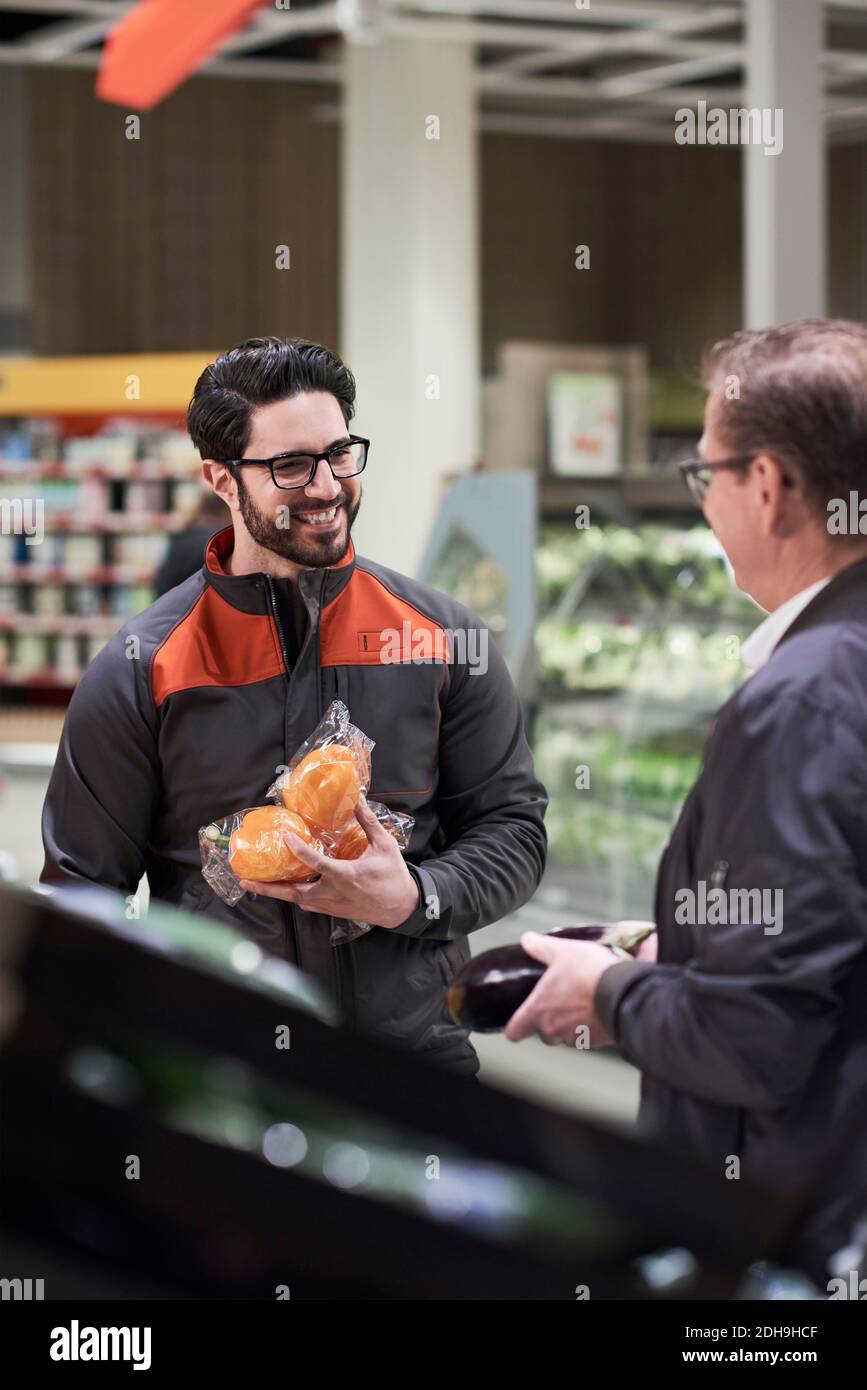 Lächelnder Verkäufer spricht Mann, während hält Gemüse im Supermarkt Stockfoto