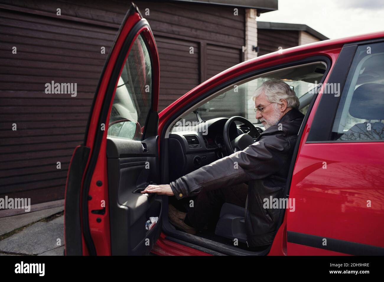 Älterer Mann, der in einem roten Auto sitzt und die Tür zuschließt Garage Stockfoto