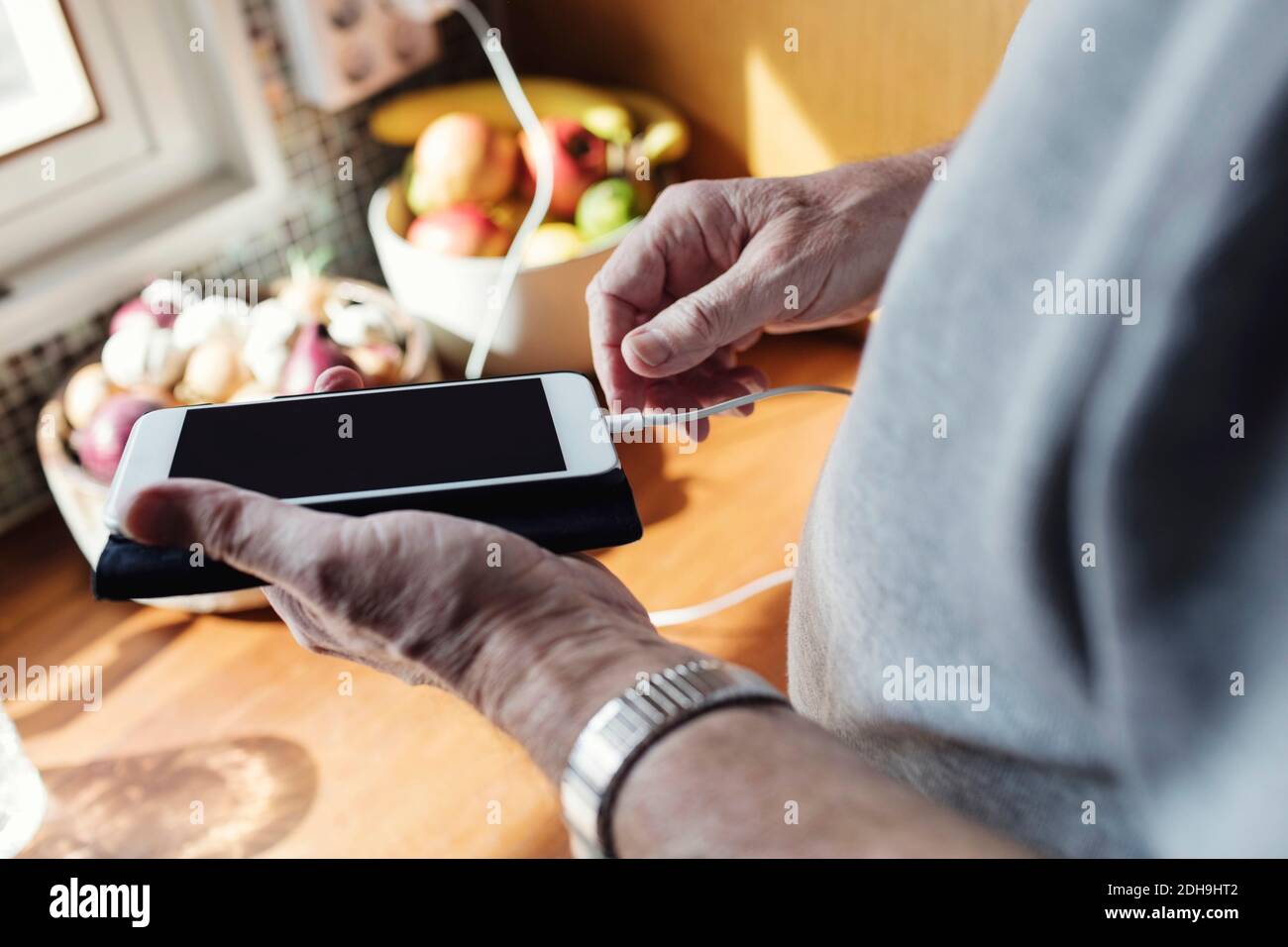 Zugeschnittenes Bild eines älteren Mannes, der das Kabel mit dem Mobiltelefon verbindet An der Küchentheke Stockfoto