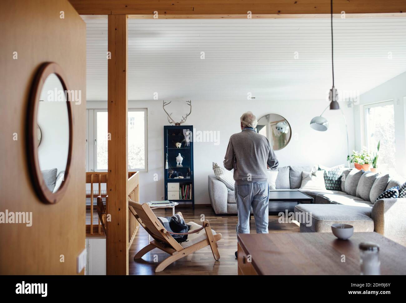 Rückansicht des älteren Mannes, der im Wohnzimmer steht Zuhause an sonnigen Tag Stockfoto