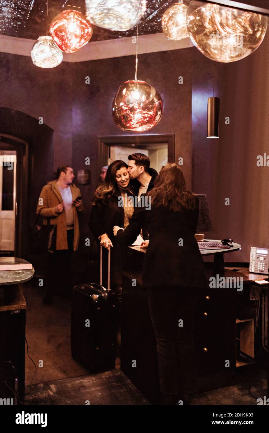 Mann küsst Freundin, während er an der Rezeption im Hotel steht Stockfoto