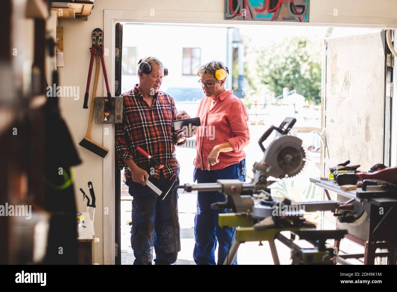 Ältere Paare, die ein digitales Tablet benutzen, während sie vor der Tür der Werkstatt stehen Stockfoto