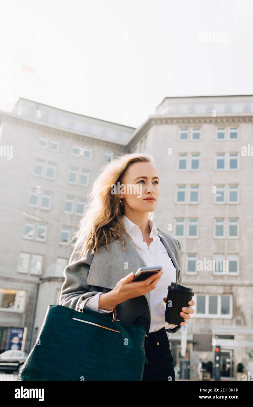 Low-Winkel-Ansicht der Kontemplation Unternehmer mit Handy suchen Entfernt, während Sie in der Stadt stehen Stockfoto