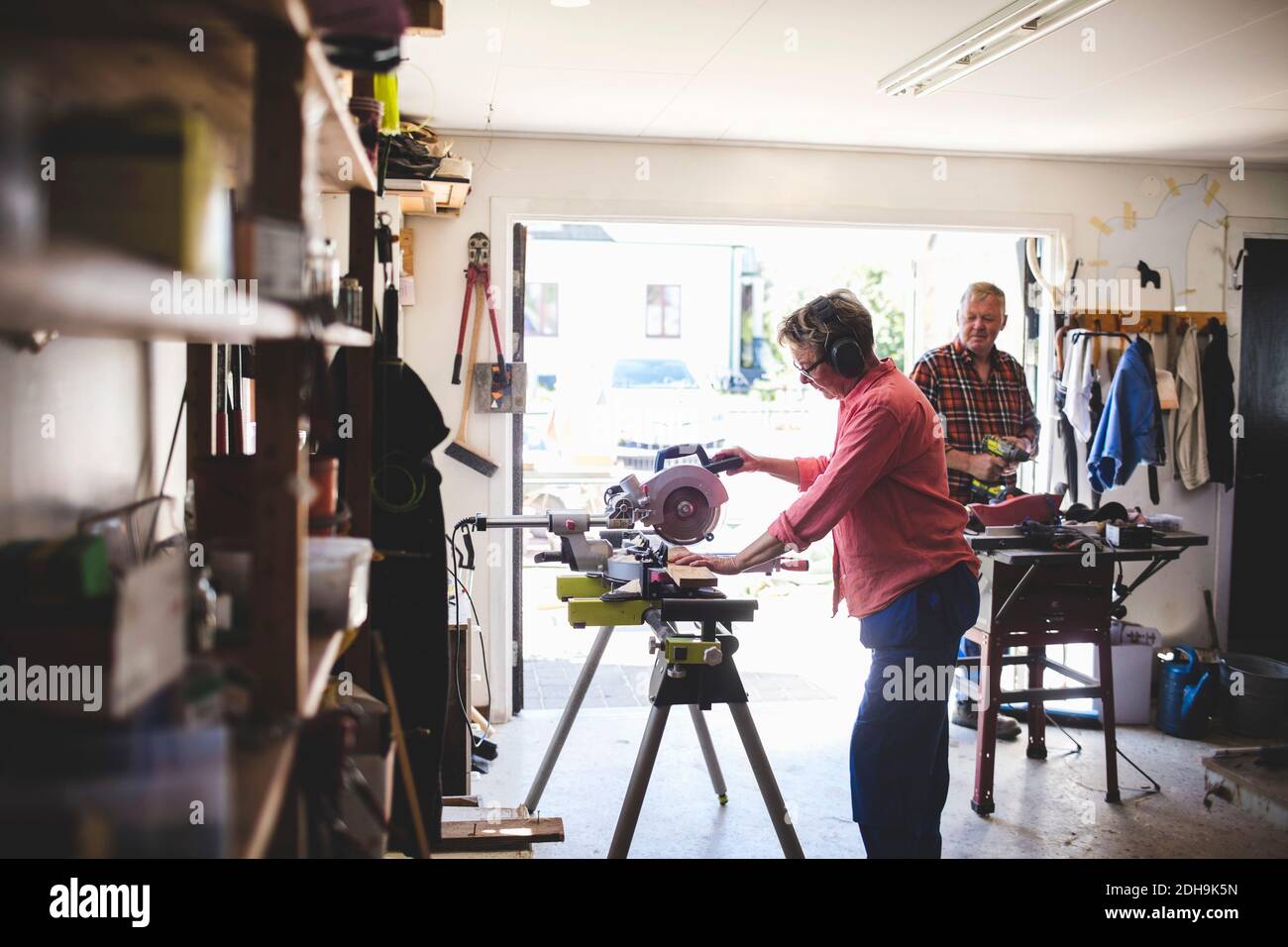 Seitenansicht der älteren Frau mit Kreissäge, während Mann Bohrer im Hintergrund halten Stockfoto