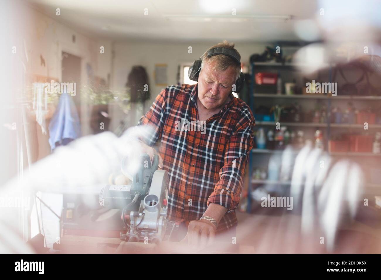 Älterer Mann mit Kreissäge in der Werkstatt durch Glas gesehen Angezeigt Stockfoto