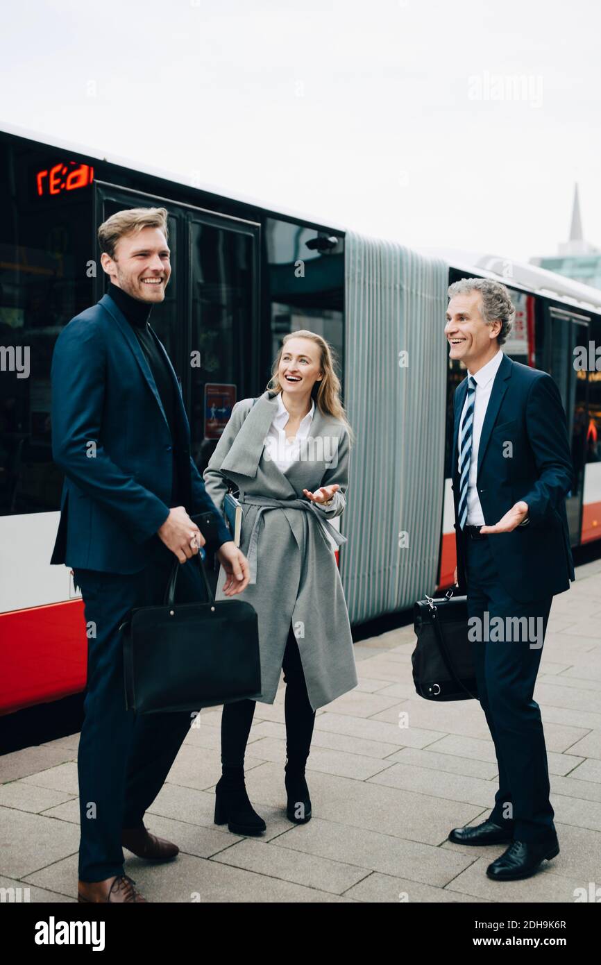Lächelnde Geschäftsfrau mit männlichen Kollegen, die in der Stadt gegen den Bus stehen Stockfoto