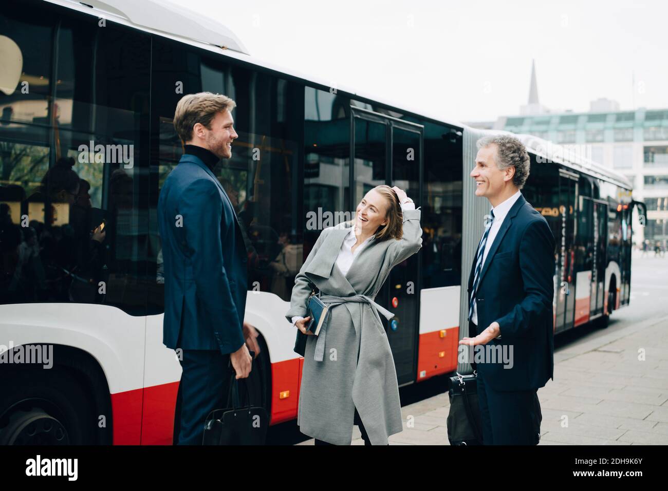 Lächelnde Geschäftsfrau mit männlichen Kollegen, die in der Stadt gegen den Bus stehen Stockfoto