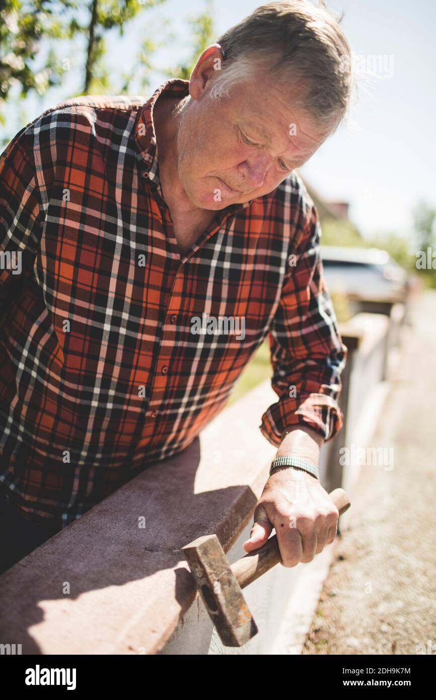 Älterer Mann, der die umgebende Wand mit Hammer auf dem Hof untersucht Stockfoto