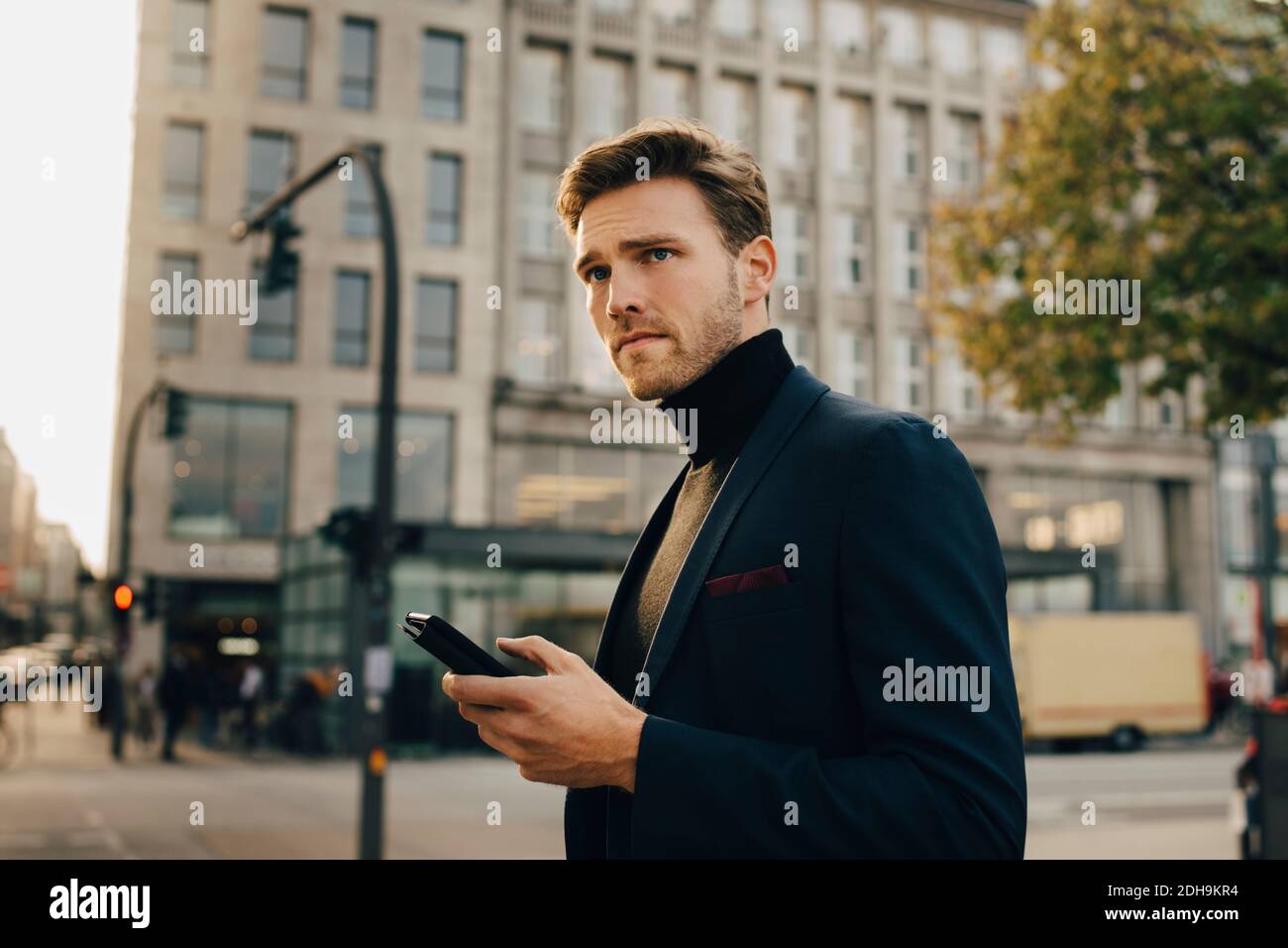 Erwägen Geschäftsmann mit Smartphone wegschauen, während sich dagegen Gebäude in der Stadt Stockfoto