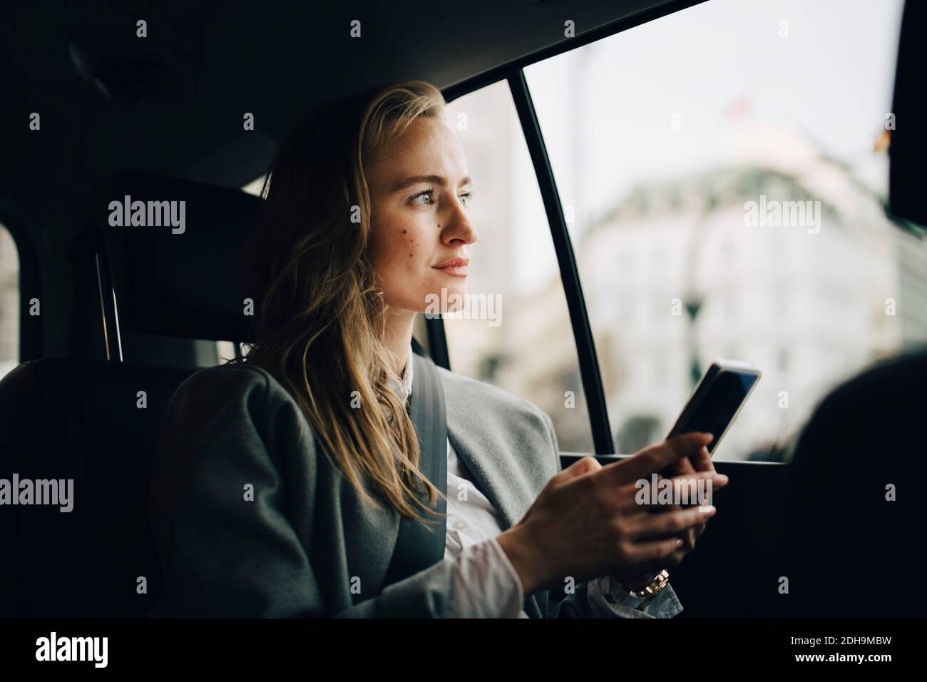 Betrachten weibliche Unternehmerin mit Smartphone Blick durch Fenster, während Sitzen im Taxi Stockfoto