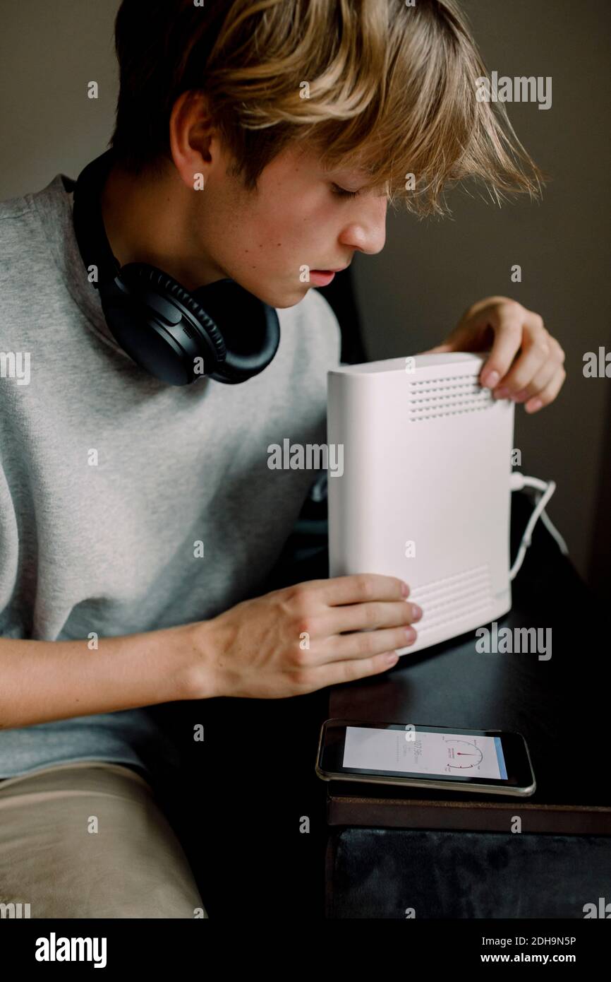 Teenager, der den WLAN-Router überprüft, während er auf dem Sofa sitzt Zu Hause Stockfoto