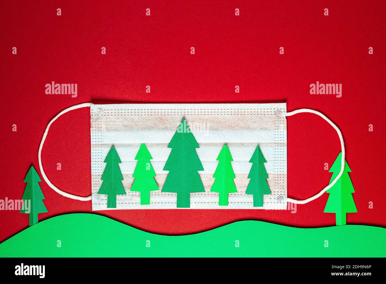Weihnachtsbäume aus Papier mit medizinischen Einweg-Gesichtsmaske auf rotem Hintergrund geschnitten. Weihnachtsbaum Papier schneiden Design-Karte. Weihnachtspapier-Craf Stockfoto