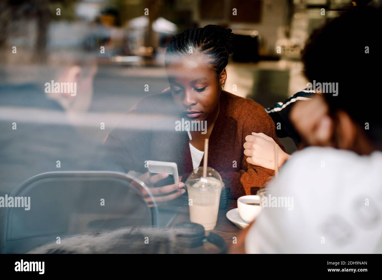 Teenager-Mädchen mit Handy, während sie mit Freunden sitzen Cafe durch Glasfenster gesehen Stockfoto