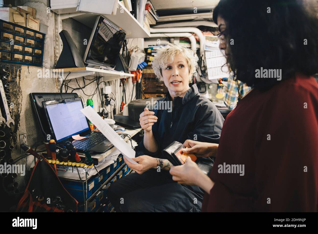 Die Mechanikerin zeigt dem Kunden, der die Kreditkarte hält, den Beleg autowerkstatt Stockfoto
