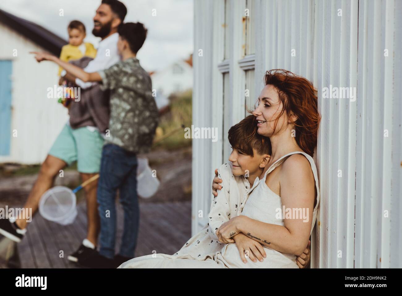 Lächelnde Mutter umarmt Sohn, während Familie im Hintergrund stehen Stockfoto