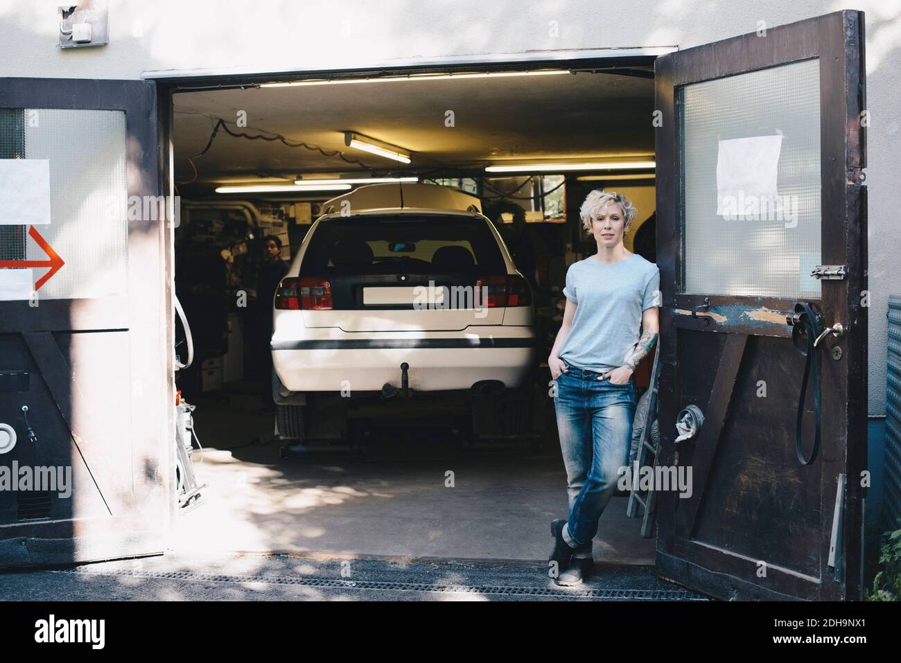 Porträt der selbstbewussten Frau lehnt sich an die Tür am Eingang von autowerkstatt Stockfoto