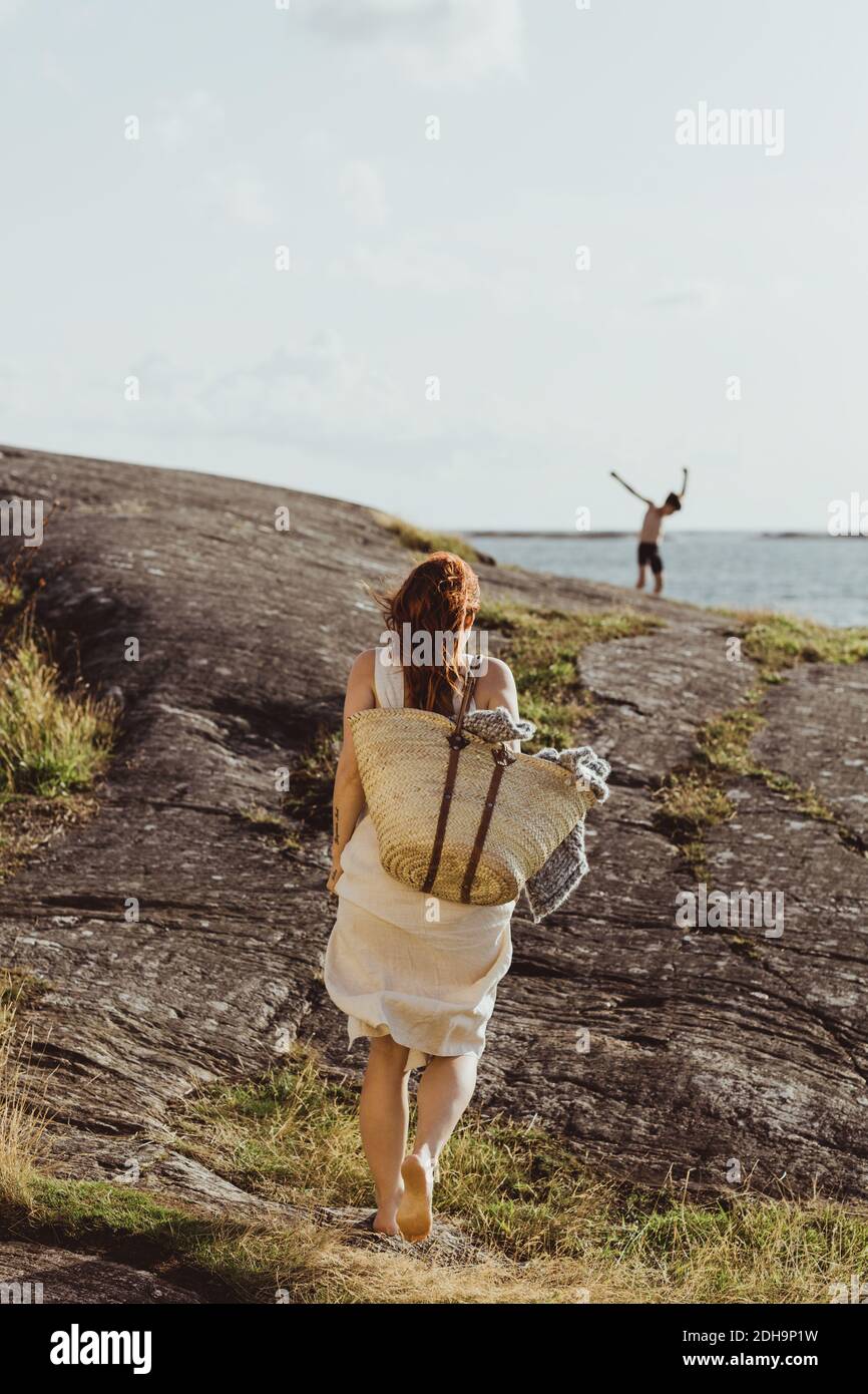 Rückansicht einer Frau mit Tasche, die auf dem Land gegen läuft Himmel an sonnigen Tagen Stockfoto