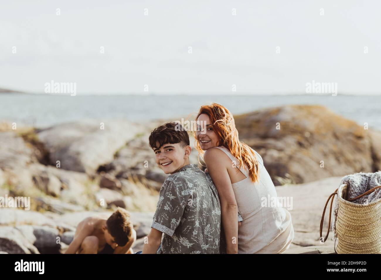 Portrait von lächelnder Mutter und Sohn, die sich beim Sitzen verbinden Felsenland an sonnigen Tagen Stockfoto