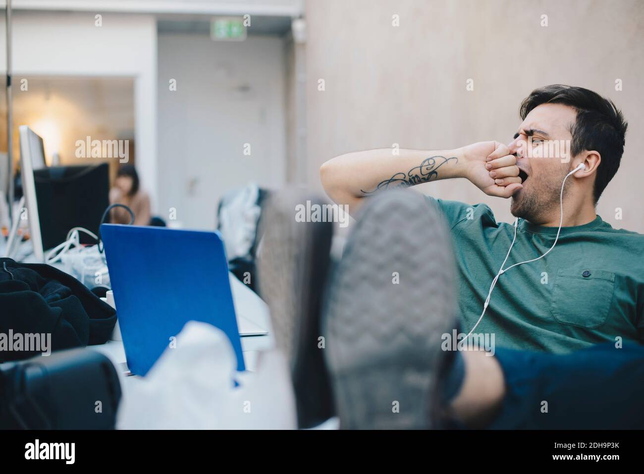 Müde Computer-Programmierer gähnend, während mit den Füßen oben sitzen Schreibtisch im Büro Stockfoto
