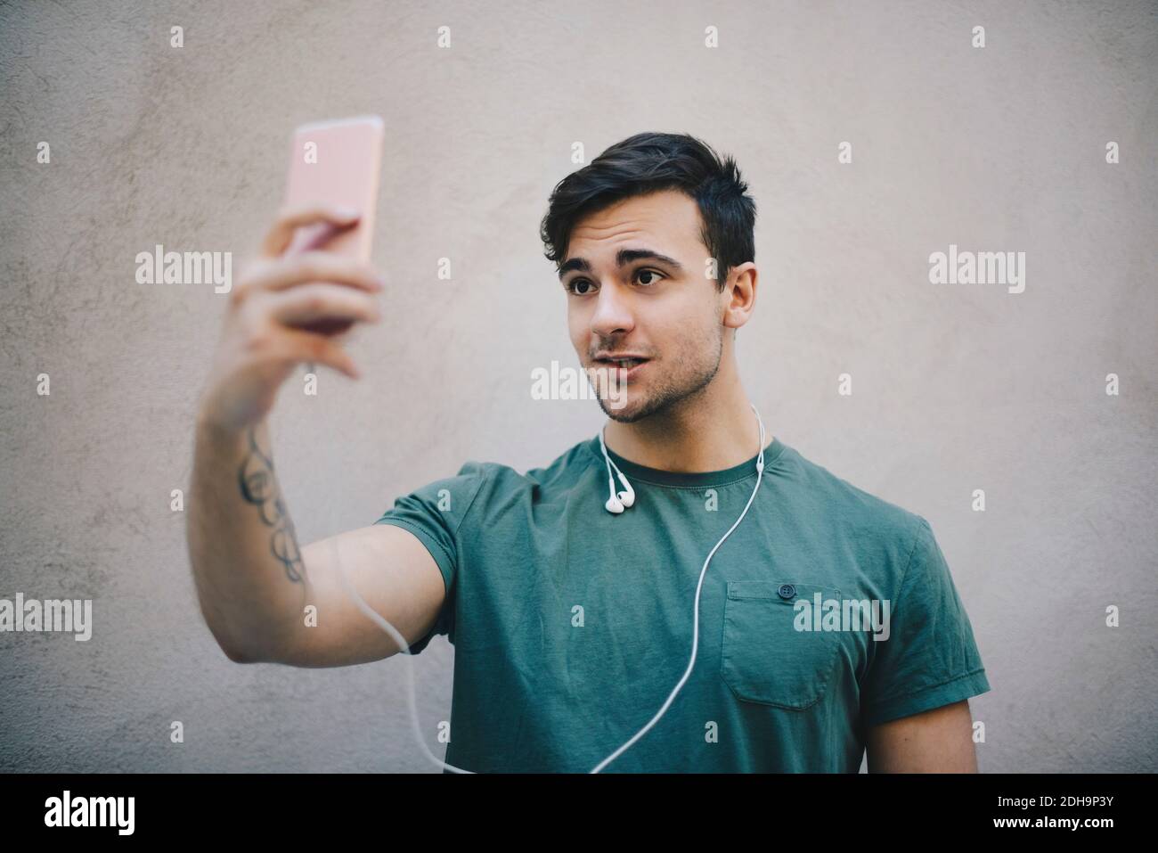 Junge männliche Computer-Programmierer unter Selfie mit Smartphone gegen Beigefarbene Wand im Büro Stockfoto