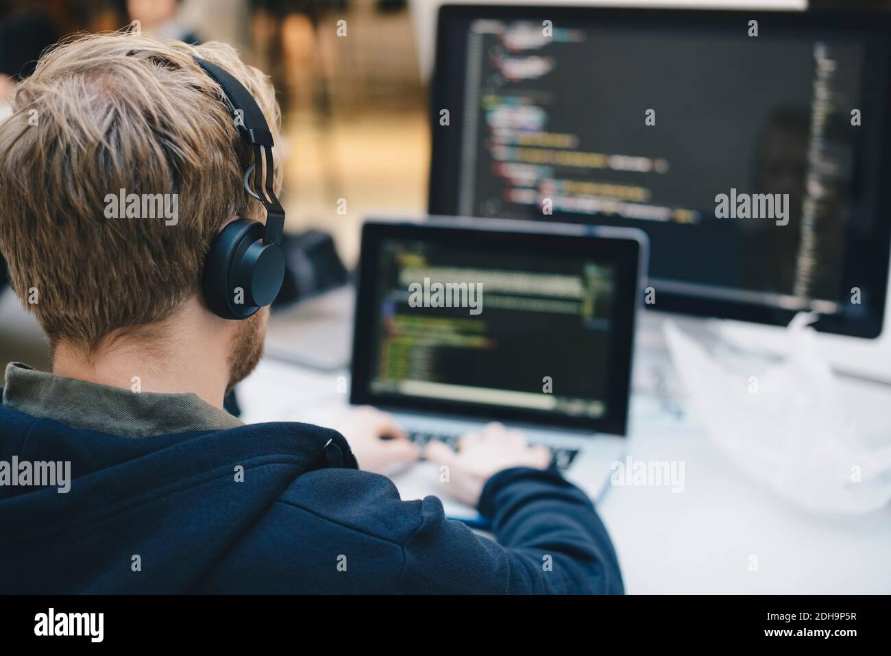 Über die Schulter des Geschäftsmannes, der Kopfhörer während der Programmierung trägt Auf dem Laptop im Kreativbüro Stockfoto