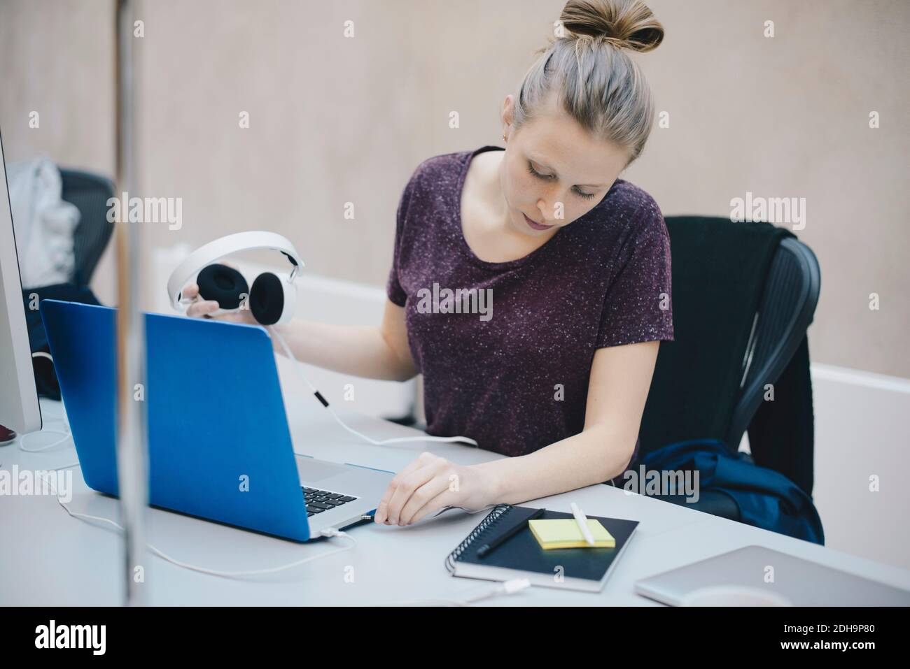 Weibliche Computerprogrammiererin, die Kopfhörer mit dem Laptop am Schreibtisch verbindet Büro Stockfoto