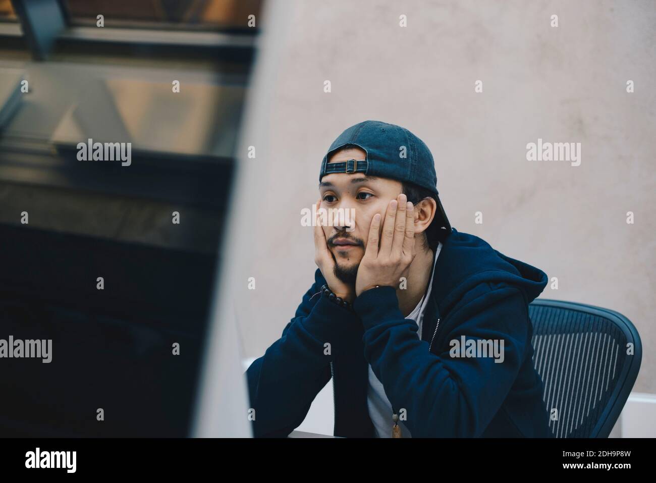 Junger Computerprogrammierer, der Computer benutzt, während er mit Kopf innen sitzt Hände im Büro Stockfoto