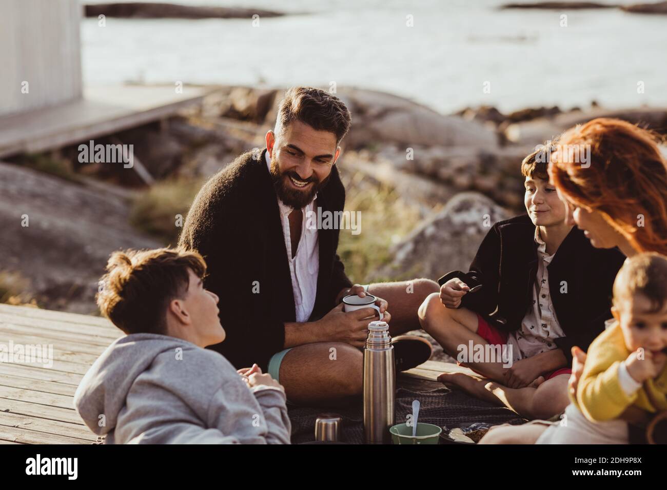 Lächelnder Vater mit Familie, die im Sommer draußen im Häuschen sitzt Stockfoto