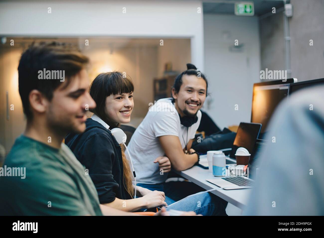 Glückliche männliche und weibliche Computerprogrammierer, die sich am Schreibtisch unterhalten Büro Stockfoto