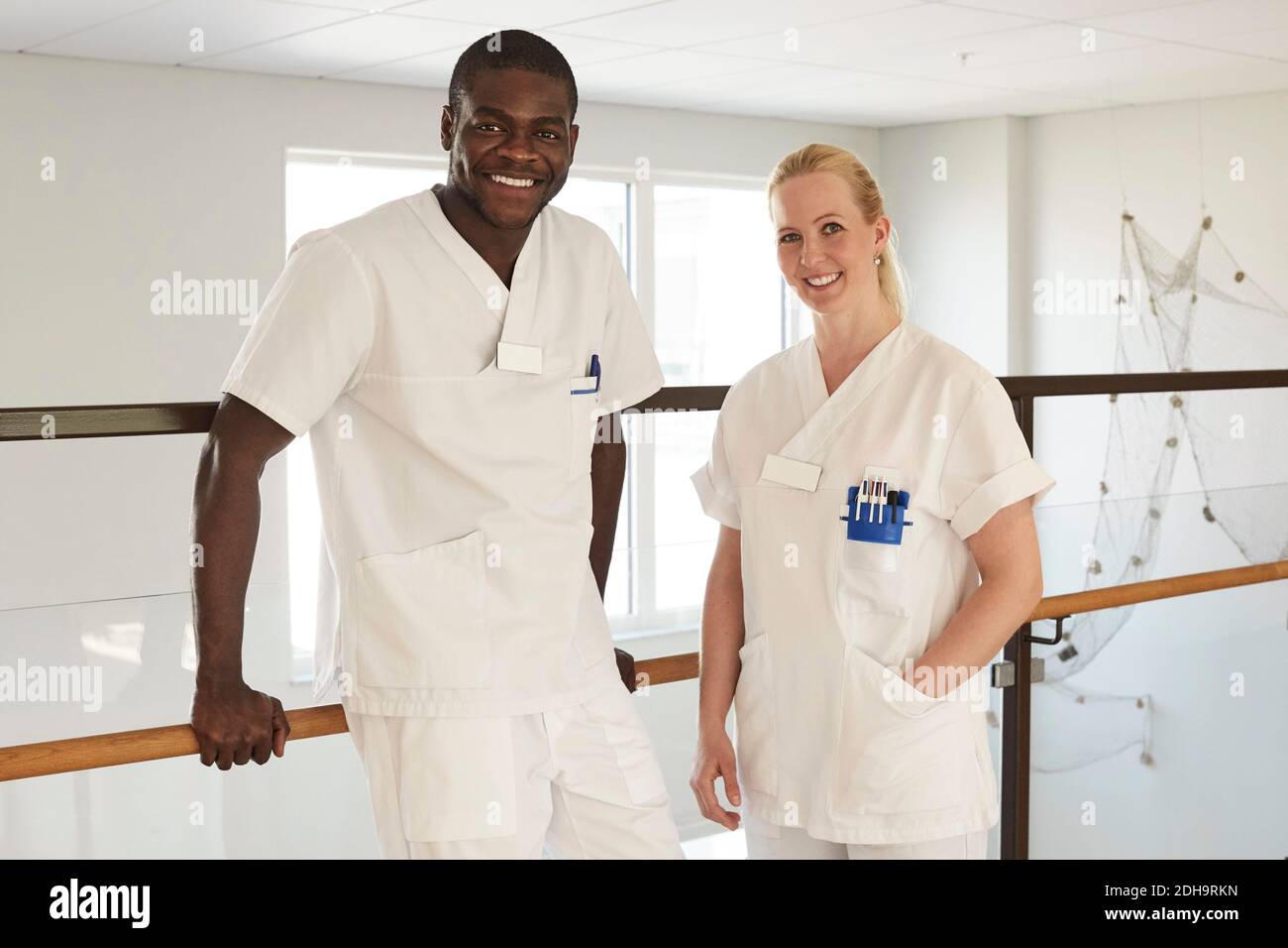 Porträt von selbstbewussten Krankenschwestern und Krankenschwestern, die gegen Geländer stehen Auf dem Krankenhausflur Stockfoto