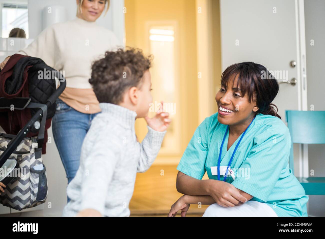 Junge im Gespräch mit lächelnden Krankenschwester, während Mutter im Stehen Hintergrund in der medizinischen Klinik Stockfoto