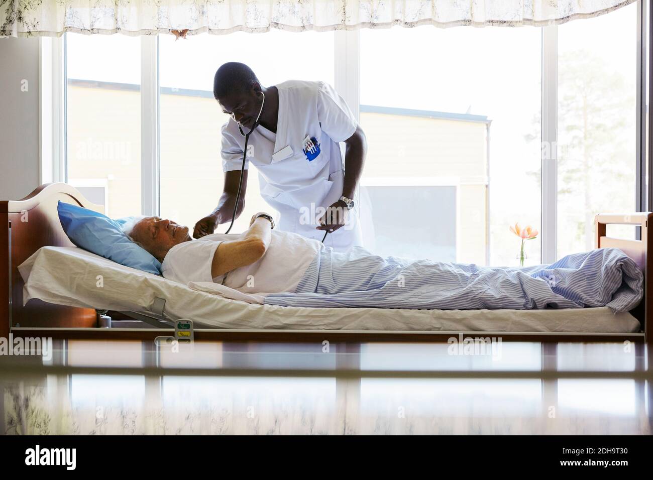 Krankenschwester untersucht älteren Mann, der auf dem Bett in hell liegend Lit. Krankenhaus Stockfoto