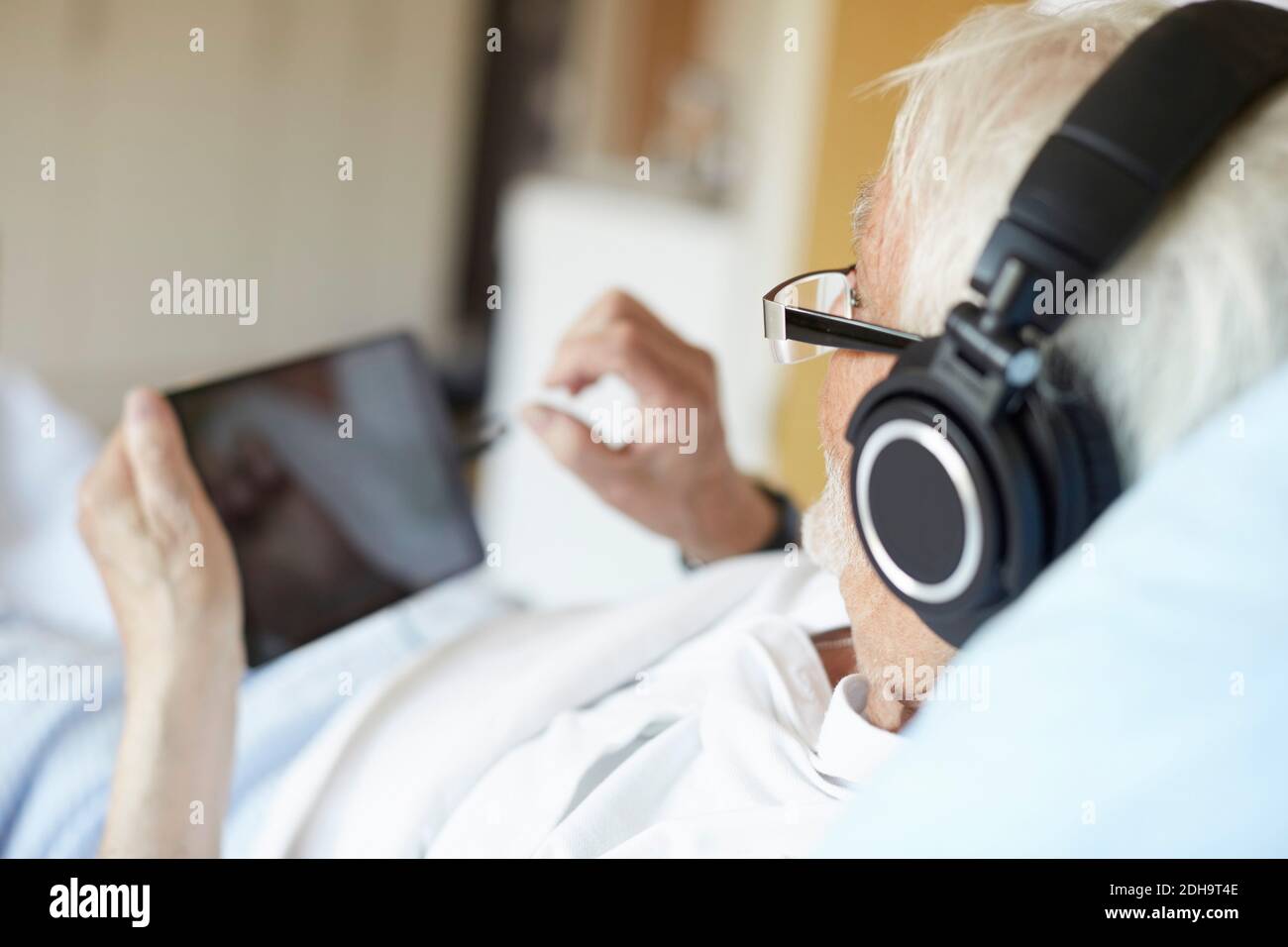 Über die Schulter des älteren Mannes, der Kopfhörer trägt, während Verwendung eines digitalen Tablets im Krankenhaus Stockfoto