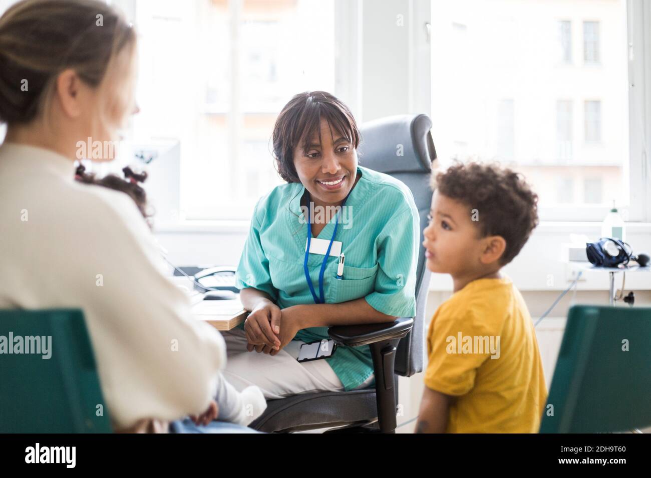 Lächelnder Kinderarzt sitzt, während Sohn Mutter im Krankenhaus anschaut Stockfoto