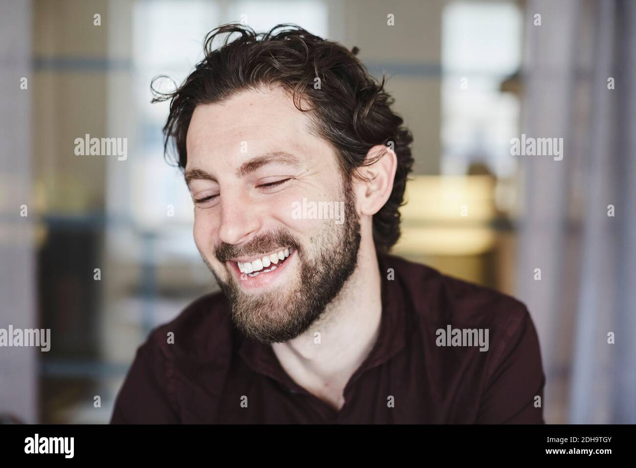 Lächelnder Geschäftsmann, der mit gekreuzten Armen an der Wellblechwand steht Im Kreativbüro Stockfoto