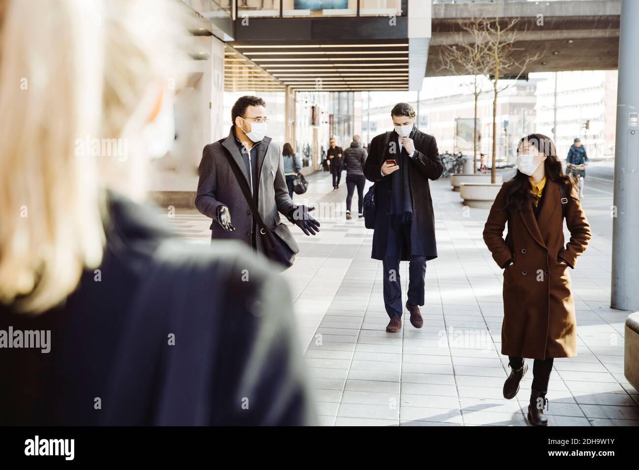 Geschäftsleute, die eine Gesichtsmaske tragen, gehen auf der Straße Stockfoto