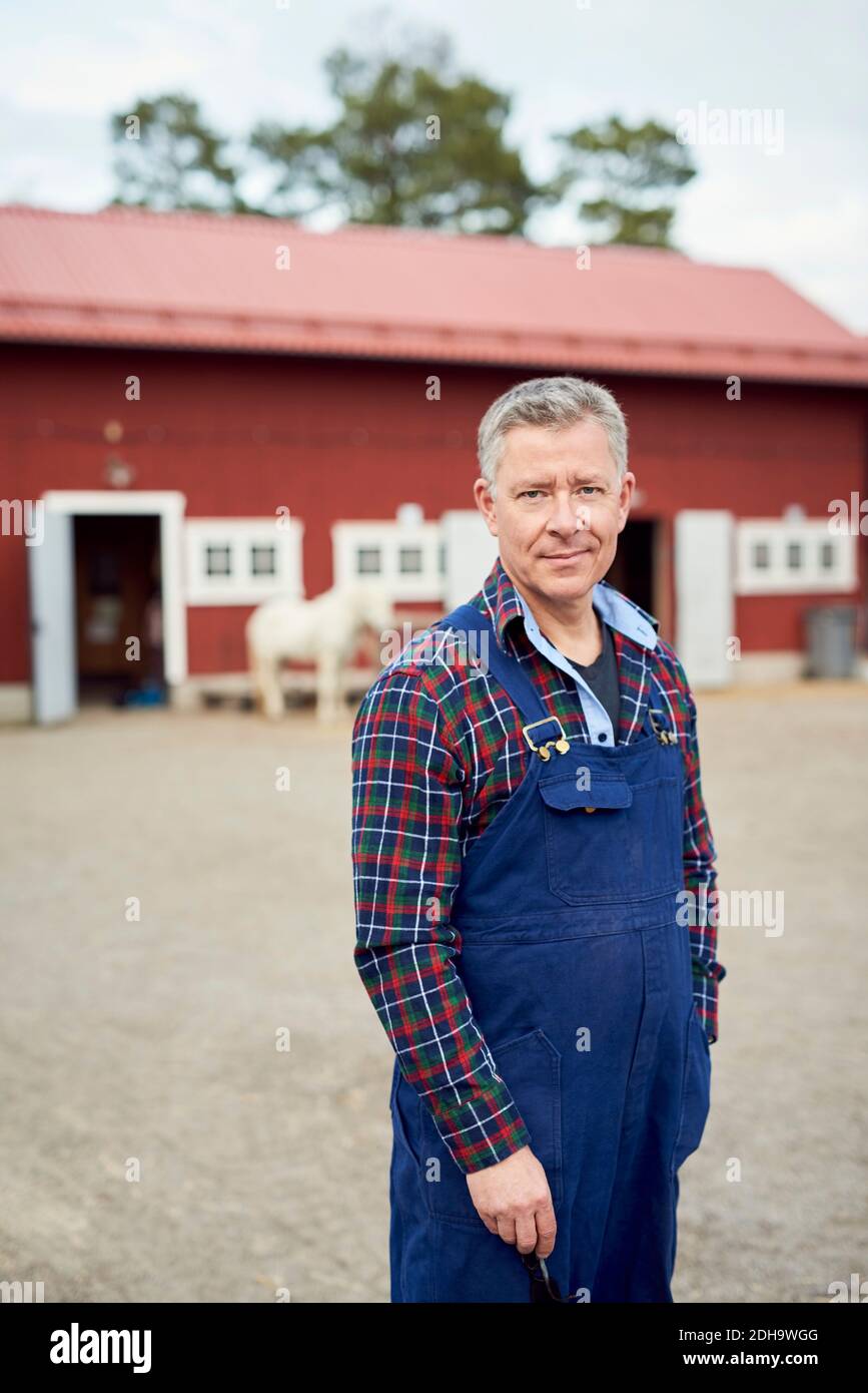 Portrait eines reifen Bauern, der auf dem Feld gegen die Scheune steht Stockfoto