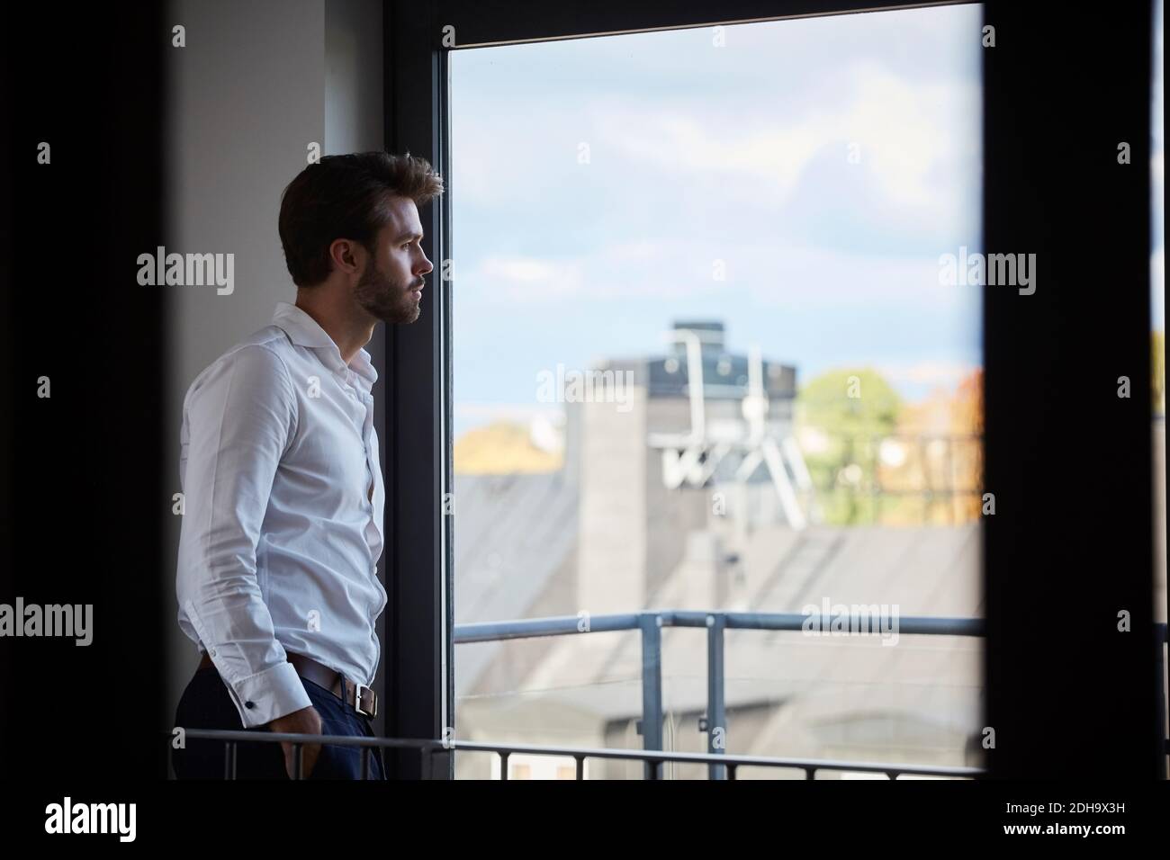 Der Geschäftsmann blickt durch das Fenster, während er am Bürofenster steht Stockfoto